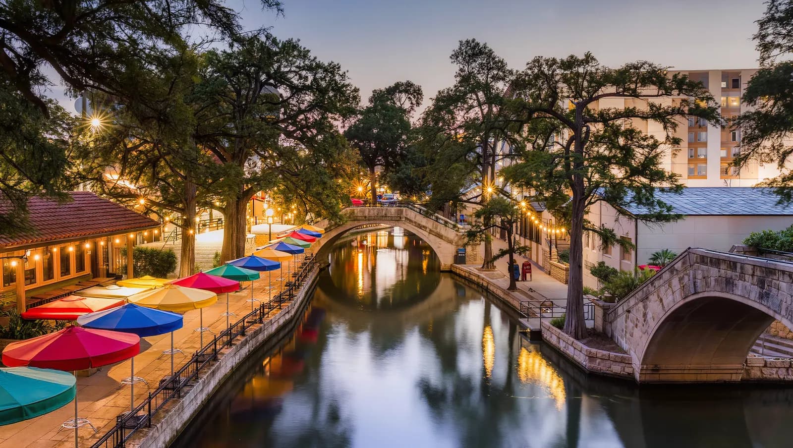 San Antonio River Walk at dusk with cypress trees and string lights